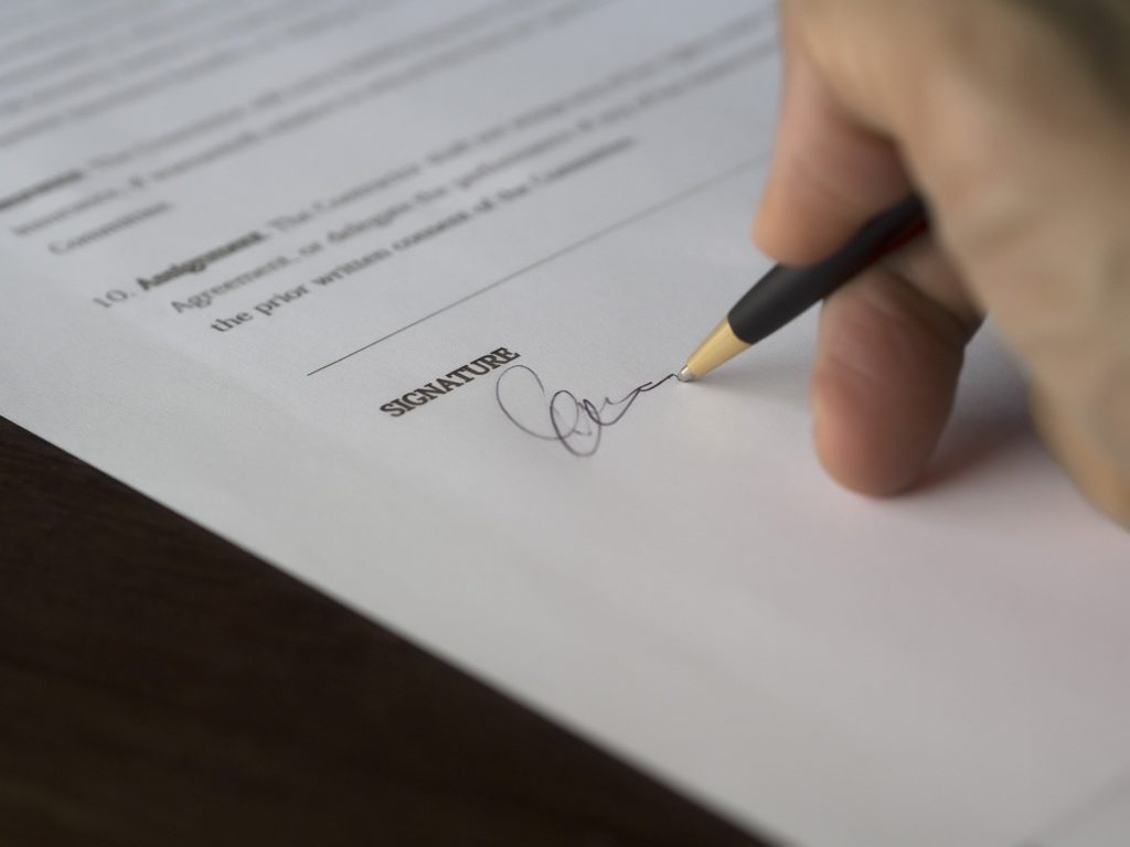 Vemos uma pessoa que assina o espaço reservado à assinatura de um contrato (imagem ilustrativa). Texto: franchising.
